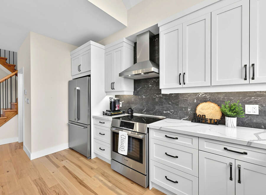 This modern kitchen boasts sleek white cabinetry paired with a striking dark marble backsplash, creating a sophisticated and contemporary aesthetic.