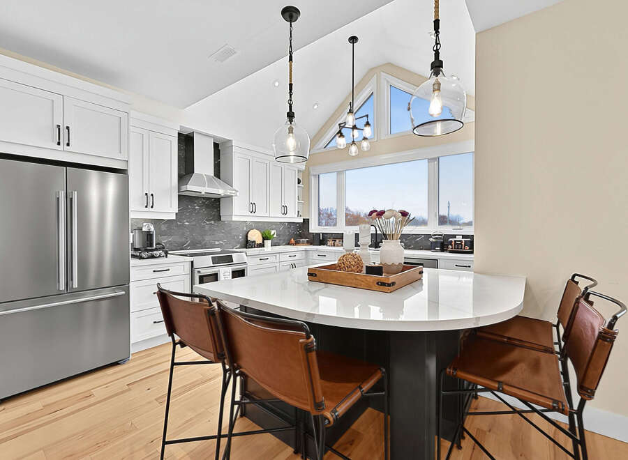 This stunning kitchen boasts sleek white cabinetry, a modern stainless steel refrigerator, and a spacious island with comfortable leather bar stools.