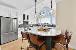 This stunning kitchen boasts sleek white cabinetry, a modern stainless steel refrigerator, and a spacious island with comfortable leather bar stools.