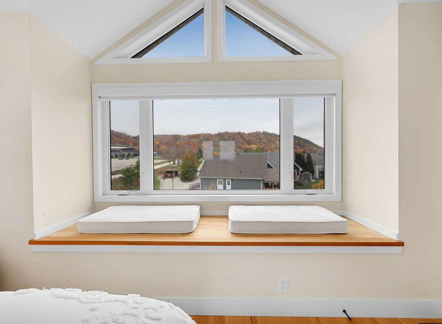 This charming bedroom features a spacious window seat with two comfortable white cushions, perfect for relaxing and enjoying the scenic autumn views.