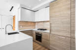 This modern kitchen features sleek white cabinetry contrasted with warm, natural wood accents on the refrigerator and lower cabinets.