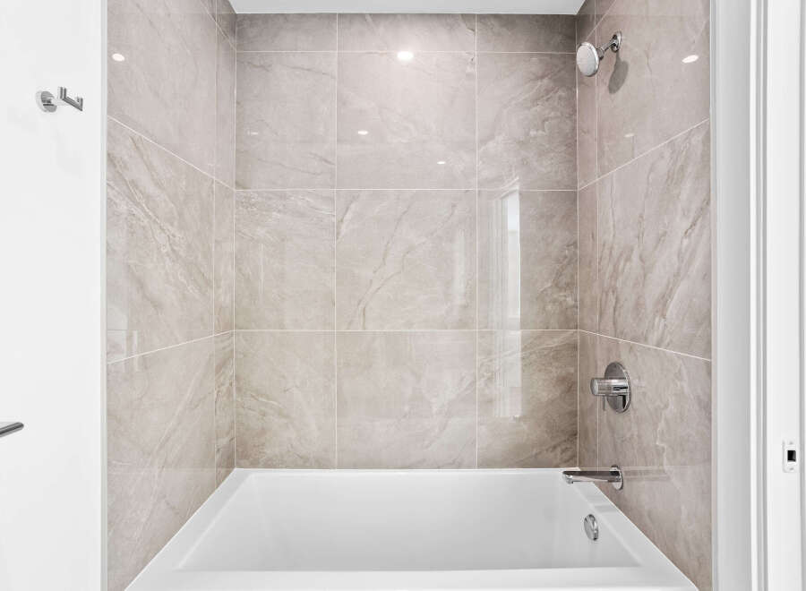 Experience modern comfort in this beautifully tiled bathroom, featuring a sleek bathtub and a rainfall showerhead for a spa-like experience.