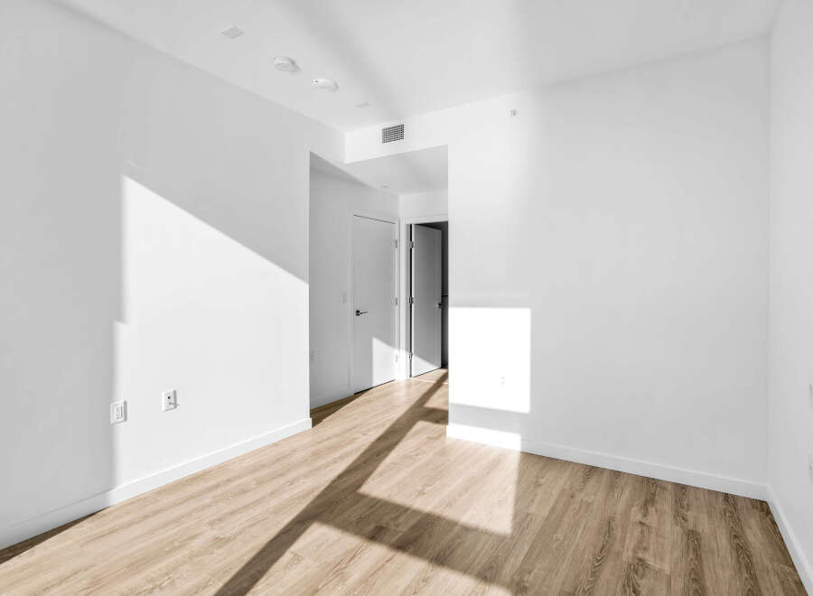 Step into this bright and airy living space, featuring pristine white walls and a modern light wood floor.