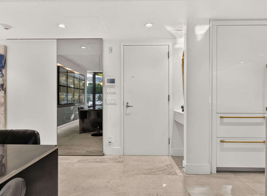 Step into a modern entryway featuring a sleek white door with brushed gold hardware, complemented by a mirrored sliding door that opens to a sophisticated dining area.