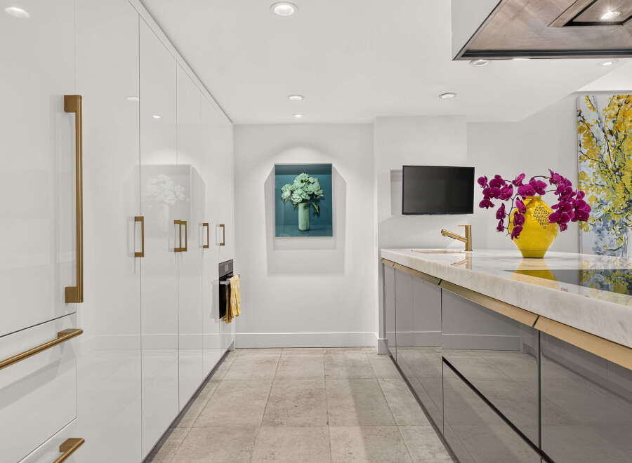 Experience luxury in this modern kitchen, featuring sleek white cabinetry with elegant brass hardware and integrated appliances.