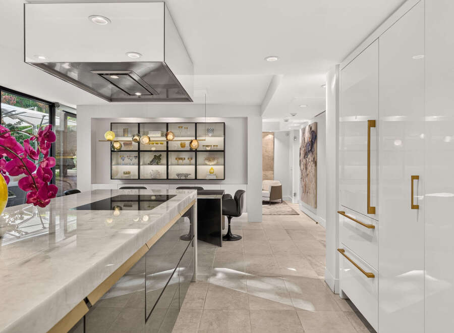 Experience modern luxury in this stunning kitchen, featuring a sleek marble island with a built-in cooktop and a sophisticated glass-front display cabinet.