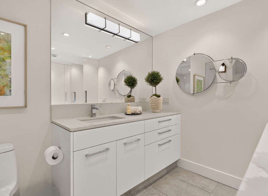 This modern bathroom features a sleek white vanity with a stone countertop and a minimalist faucet.