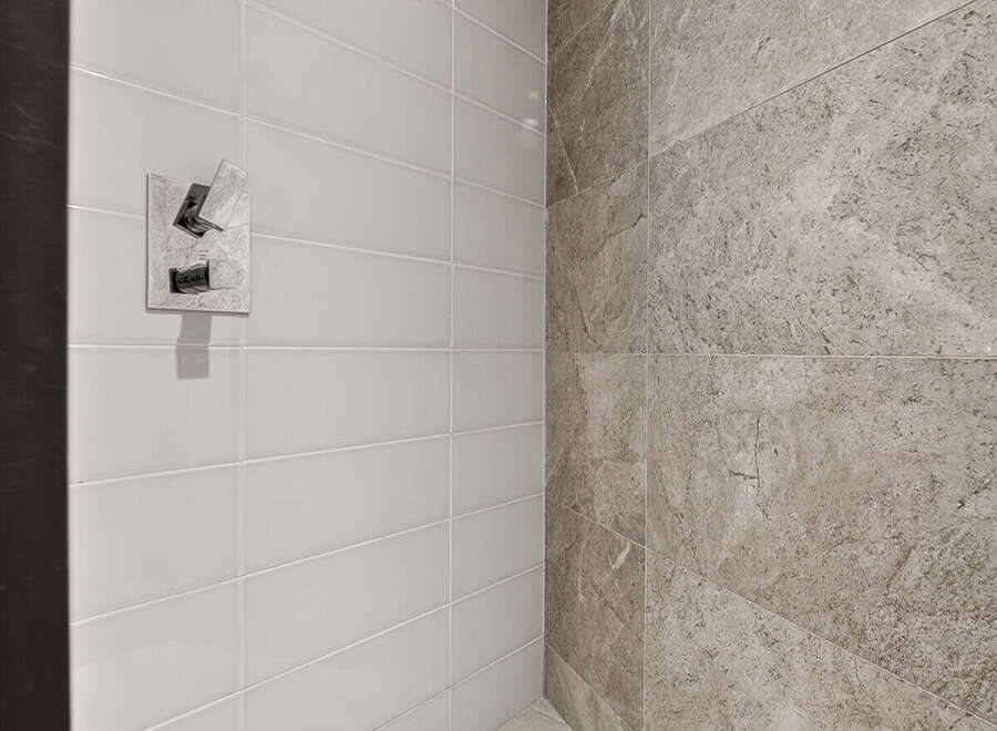 Step into this modern shower featuring sleek white subway tiles on one wall and elegant grey marble tiles on the adjacent wall.