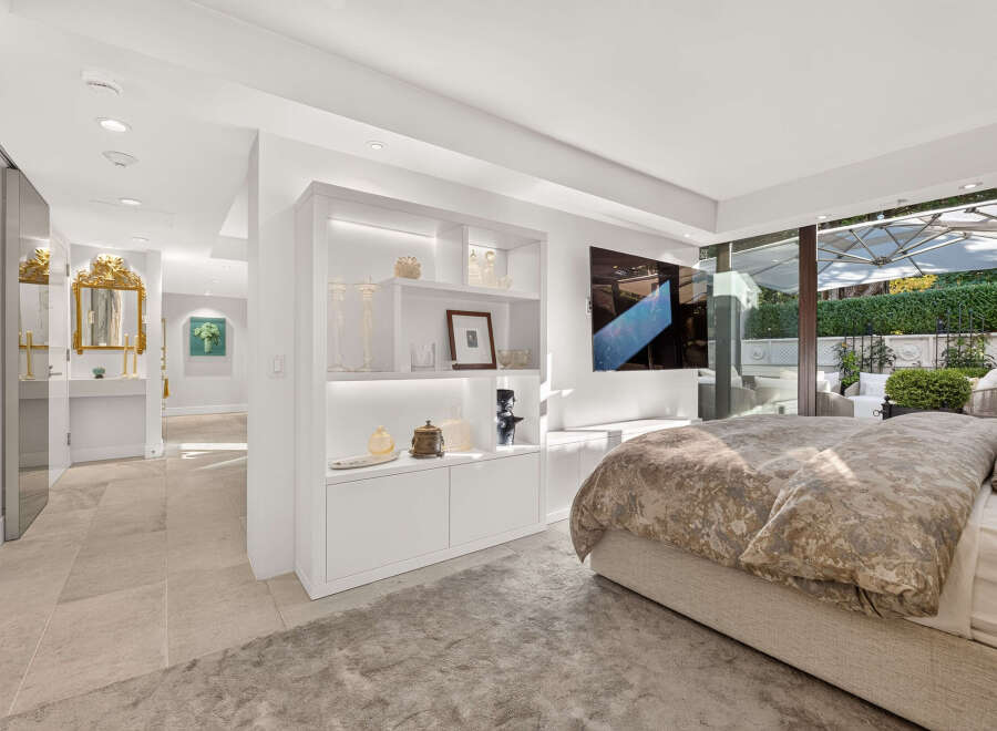 Experience luxury living in this master suite, featuring a king-sized bed with a designer duvet and a wall-mounted flat-screen TV.