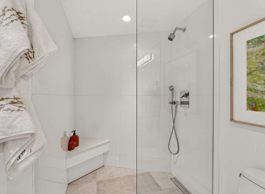Experience luxury in this modern bathroom featuring a spacious glass-enclosed shower with a built-in bench and a sleek rainfall showerhead.