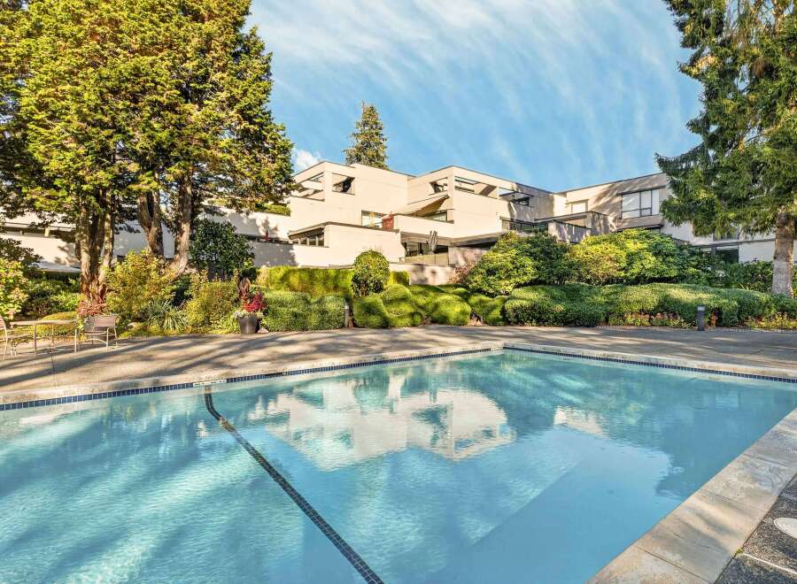 Enjoy a refreshing dip in the sparkling blue swimming pool, surrounded by lush greenery and mature trees.