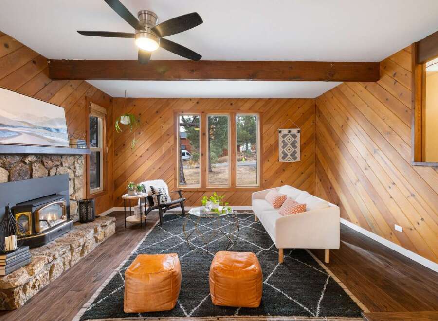 Cozy living room featuring a stone fireplace with a wood-burning insert, complemented by warm wood-paneled walls and exposed beams.
