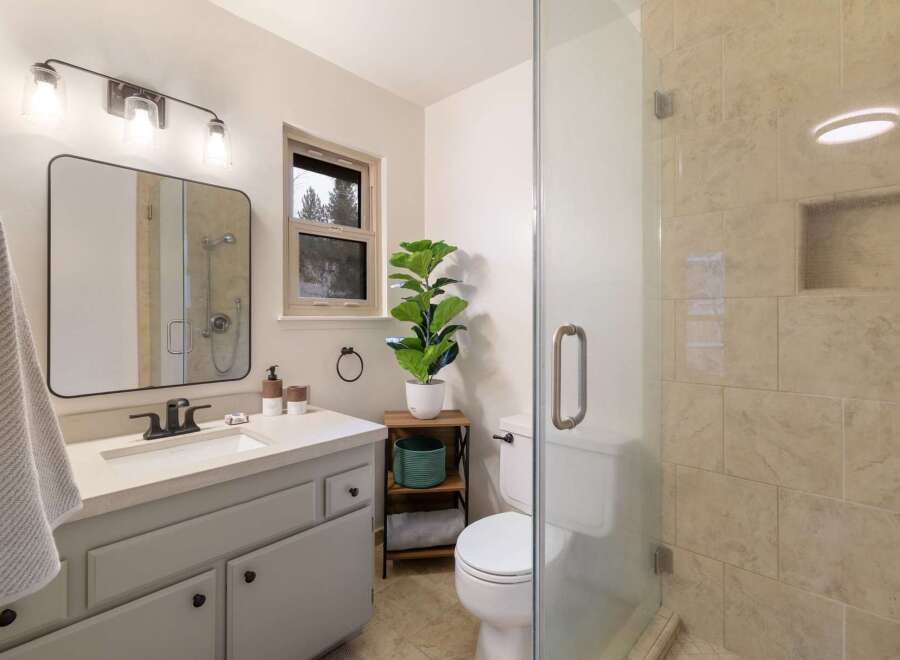 This charming bathroom features a modern vanity with ample storage and a sleek black faucet, complemented by a large, rounded mirror.