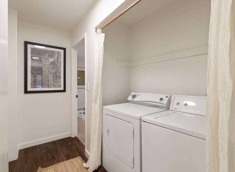 This hallway features a modern laundry area with a white washer and dryer, discreetly hidden by a light-colored curtain.