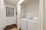 This hallway features a modern laundry area with a white washer and dryer, discreetly hidden by a light-colored curtain.