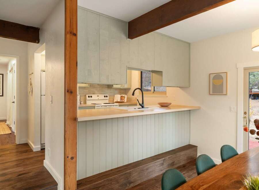 This charming kitchen features light green paneled cabinets and a butcher block countertop, creating a warm and inviting atmosphere.