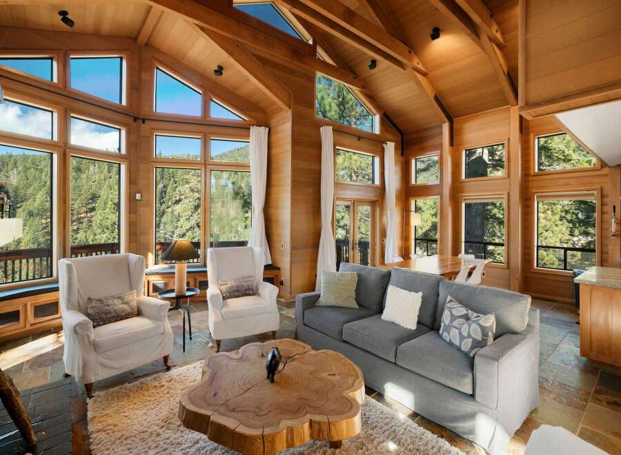 Experience breathtaking mountain views from this stunning living room, featuring a soaring vaulted ceiling with exposed wooden beams and expansive windows that flood the space with natural light.