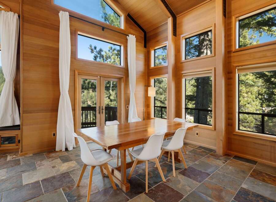 Experience breathtaking natural beauty from this stunning dining room, featuring floor-to-ceiling wood paneling and expansive windows that frame lush forest views.