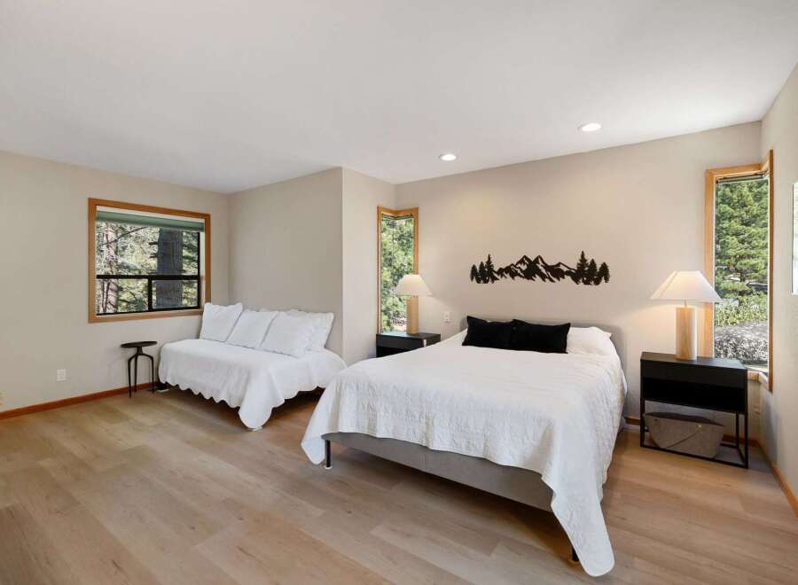 This spacious bedroom offers a comfortable king-size bed with a textured white comforter and two black accent pillows, complemented by a matching white daybed.