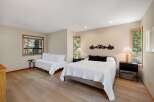 This spacious bedroom offers a comfortable king-size bed with a textured white comforter and two black accent pillows, complemented by a matching white daybed.