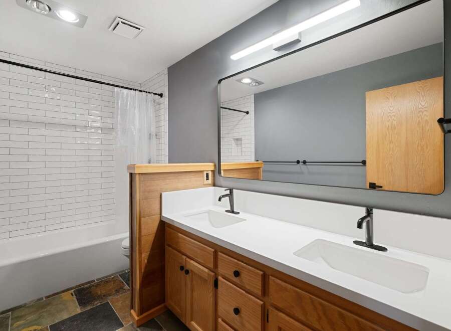 This modern bathroom features a spacious double vanity with white quartz countertops and warm wood cabinetry, complemented by sleek black fixtures.