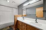 This modern bathroom features a spacious double vanity with white quartz countertops and warm wood cabinetry, complemented by sleek black fixtures.