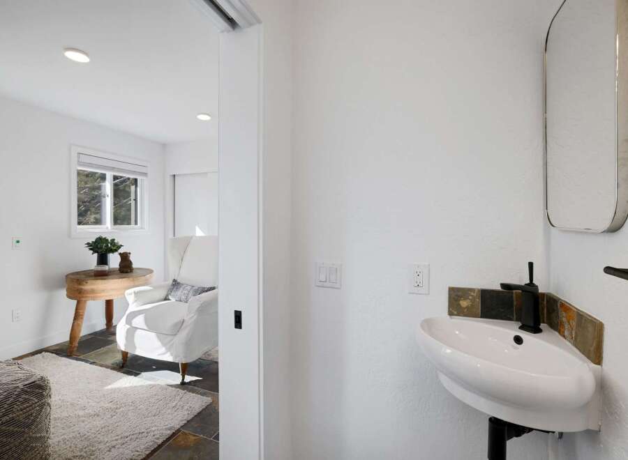 This charming space features a bright and airy living area with a comfortable armchair and a rustic wooden side table, perfect for relaxation.