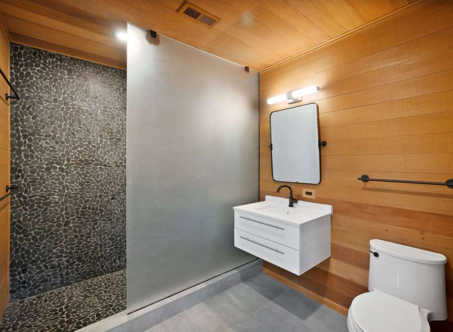 Experience a spa-like retreat in this modern bathroom, featuring a unique pebble-tiled shower and a sleek floating vanity.