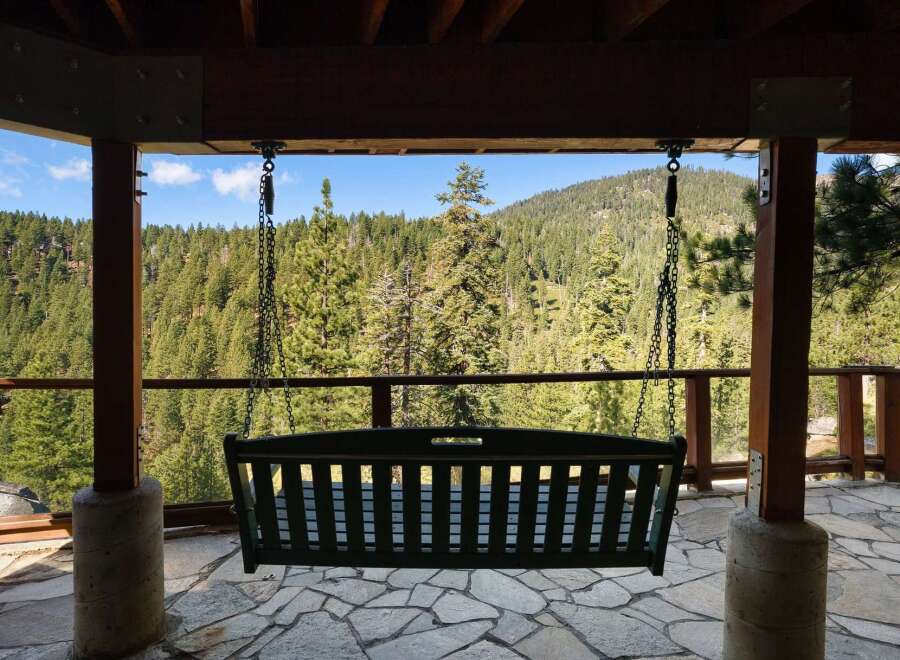 Enjoy breathtaking mountain views from this charming porch swing, perfect for relaxing and taking in the serene forest landscape.