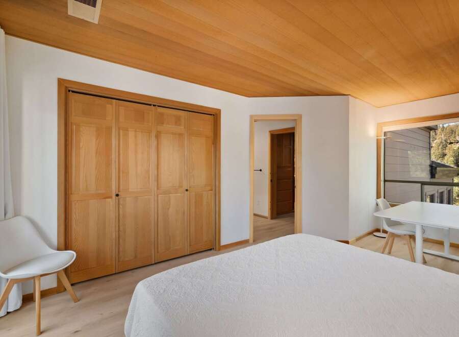 This bedroom offers a warm and inviting atmosphere with its natural wood accents, including a stunning wood-paneled ceiling and a large wooden closet.