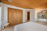 This bedroom offers a warm and inviting atmosphere with its natural wood accents, including a stunning wood-paneled ceiling and a large wooden closet.