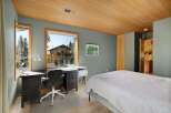 This bedroom offers a functional workspace with a large desk, an ergonomic chair, and a printer, all overlooking a scenic view of the surrounding nature and a charming house.