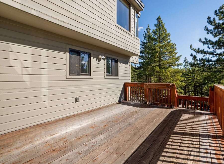 Enjoy the outdoors from this expansive wooden deck, perfect for entertaining or relaxing amidst the scenic beauty of mature pine trees.