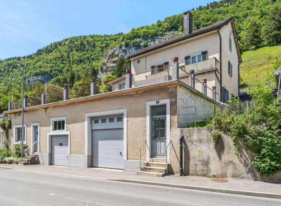 Discover this charming property nestled against a lush green mountainside, offering a unique blend of residential living and practical garage space.