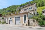 Discover this charming property nestled against a lush green mountainside, offering a unique blend of residential living and practical garage space.
