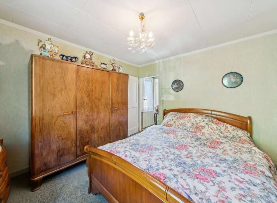 Step into a charming bedroom featuring a large, vintage wooden wardrobe and a cozy bed adorned with a floral comforter.