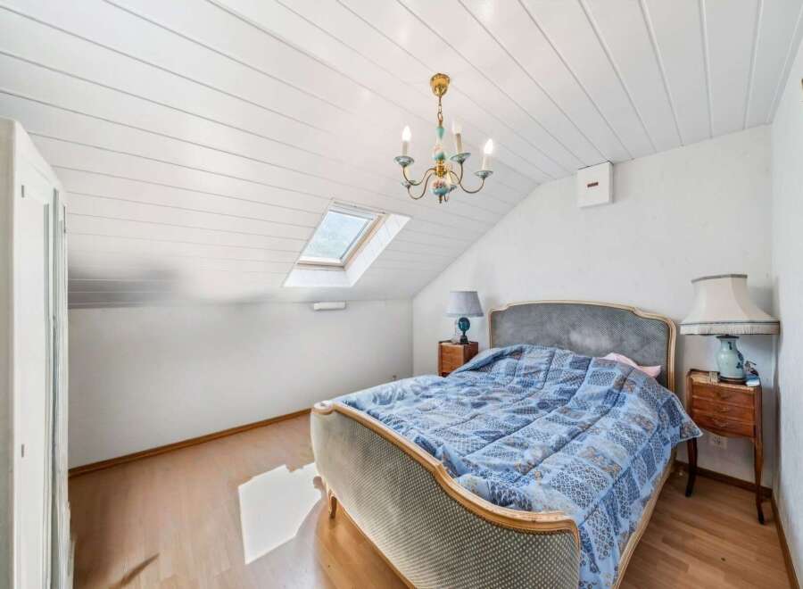 This charming attic bedroom features a comfortable bed adorned with a blue patterned comforter, perfect for a cozy retreat.