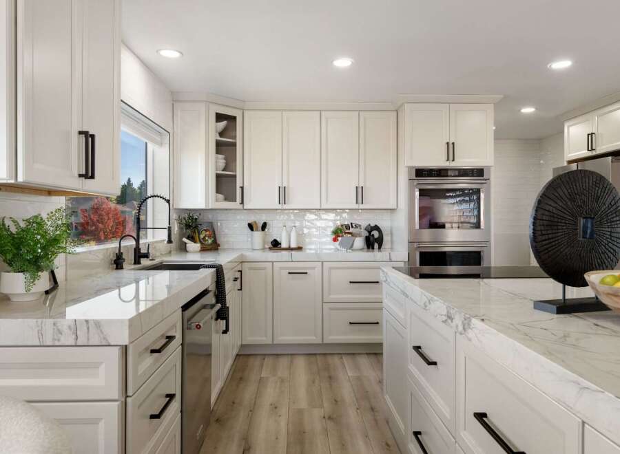 This modern white kitchen boasts sleek cabinetry with black hardware, complemented by stunning marble countertops and a subway tile backsplash.