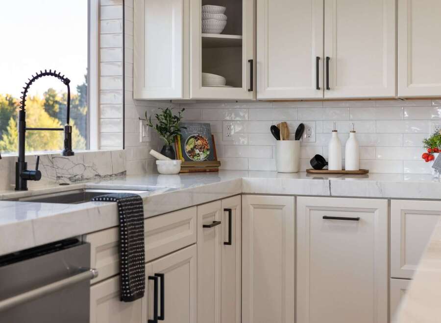 This modern kitchen boasts sleek white cabinetry with black hardware, complemented by a stunning marble countertop and backsplash.