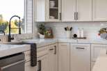 This modern kitchen boasts sleek white cabinetry with black hardware, complemented by a stunning marble countertop and backsplash.
