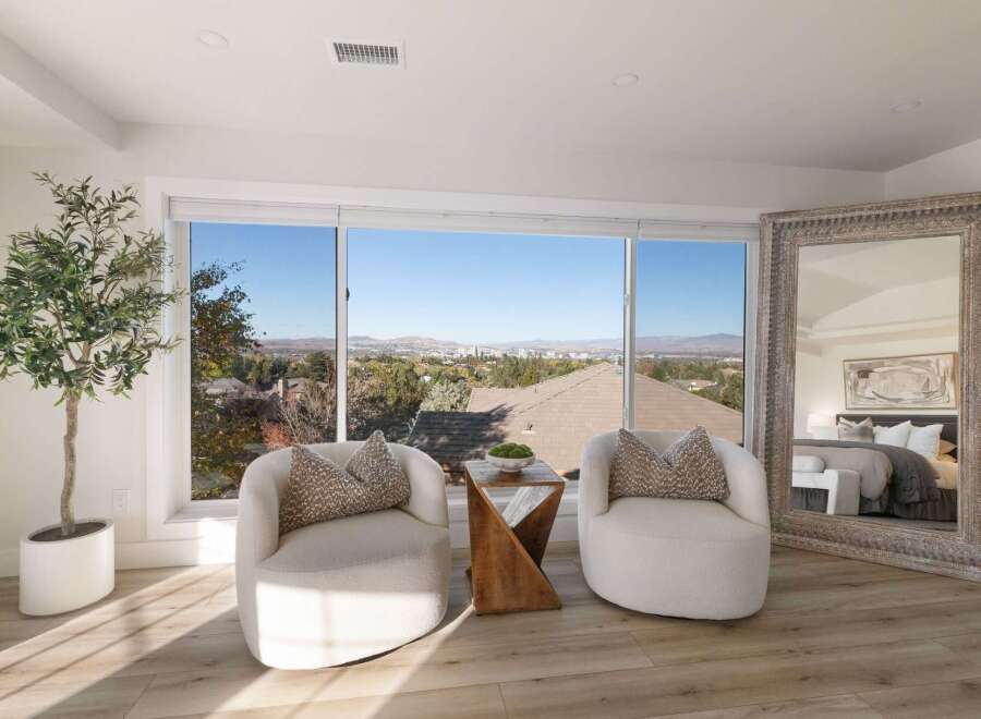Enjoy breathtaking panoramic views from this stunning bedroom, featuring a cozy seating area with two plush armchairs and a unique wooden side table.