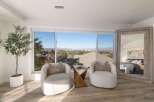 Enjoy breathtaking panoramic views from this stunning bedroom, featuring a cozy seating area with two plush armchairs and a unique wooden side table.