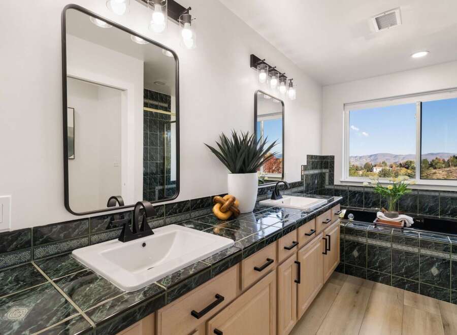 This spacious bathroom boasts a double vanity with elegant black fixtures and a stunning green marble countertop.