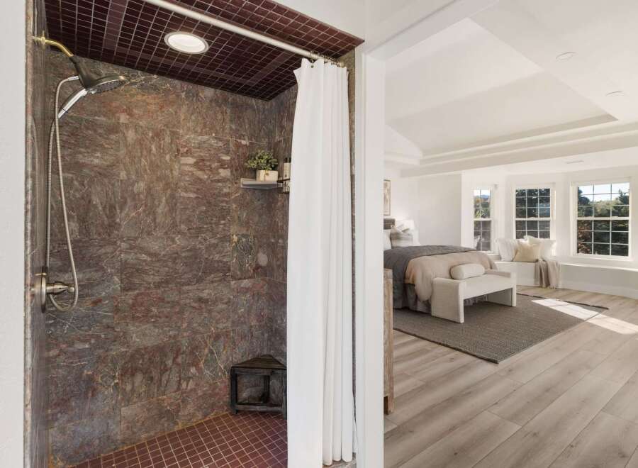 Experience luxury in this master suite featuring a spa-like shower with rich, veined stone tile and a modern showerhead.