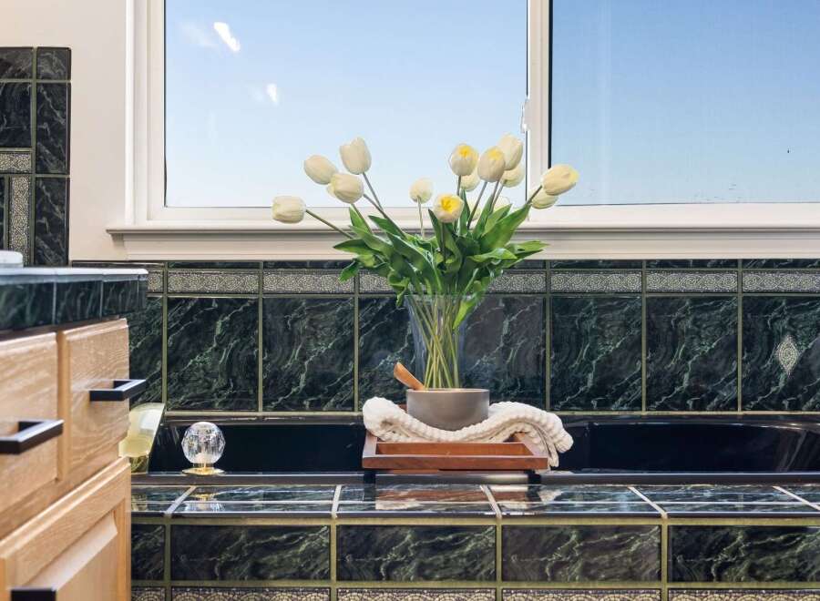 This luxurious bathroom features elegant dark green marble tiling that extends from the countertops to the bathtub surround.