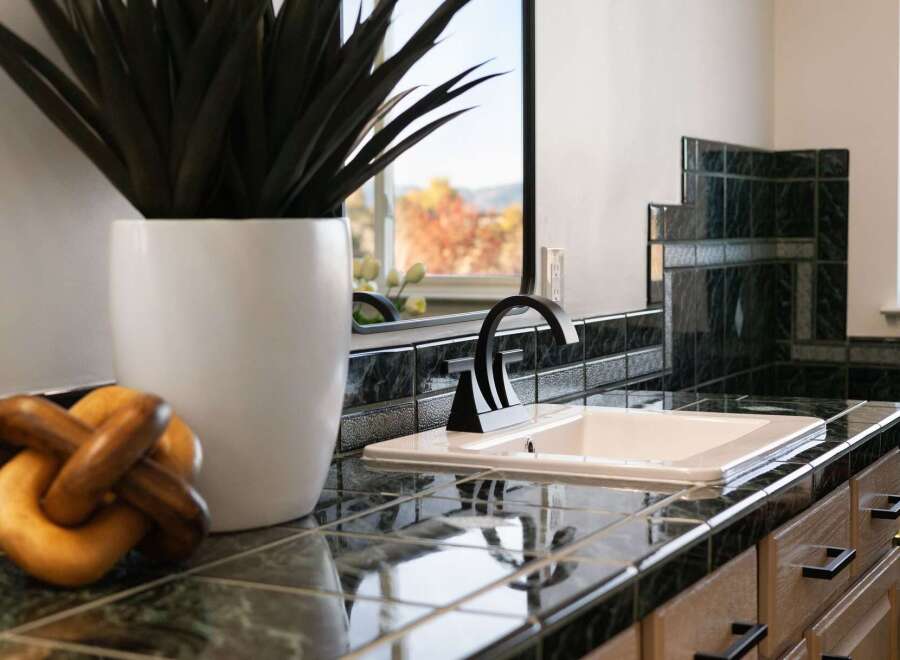 This bathroom features a sleek black faucet and a white sink set against a dark, glossy tiled backsplash and countertop.
