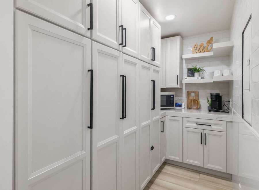 This modern kitchen features sleek white cabinetry with black hardware, offering ample storage and a clean aesthetic.