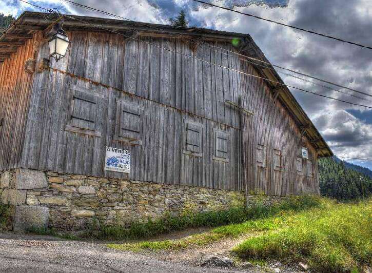 Rustic wooden barn for sale, boasting a charming stone foundation and picturesque mountain views.