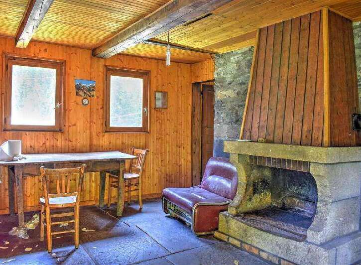 Rustic mountain cabin with wood-paneled walls, stone fireplace, and large windows offering scenic views.