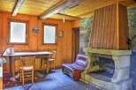 Rustic mountain cabin with wood-paneled walls, stone fireplace, and large windows offering scenic views.